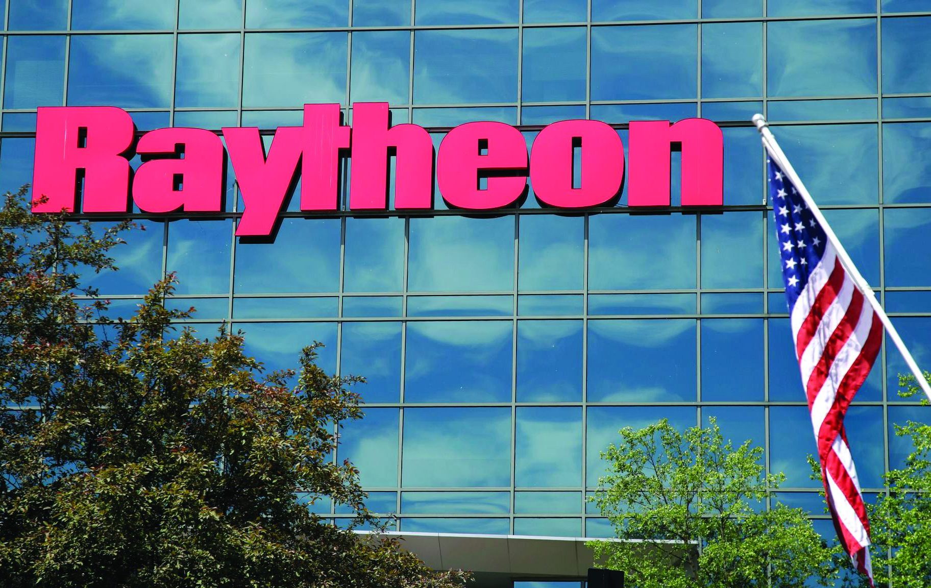 And American flag flies in front of the facade of Raytheon's Integrated Defense Systems facility, Monday, June 10, 2019, in Woburn, Mass. Raytheon Co. and United Technologies Corp. are merging in a deal that creates one of the world's largest defense companies. (AP Photo/Elise Amendola)