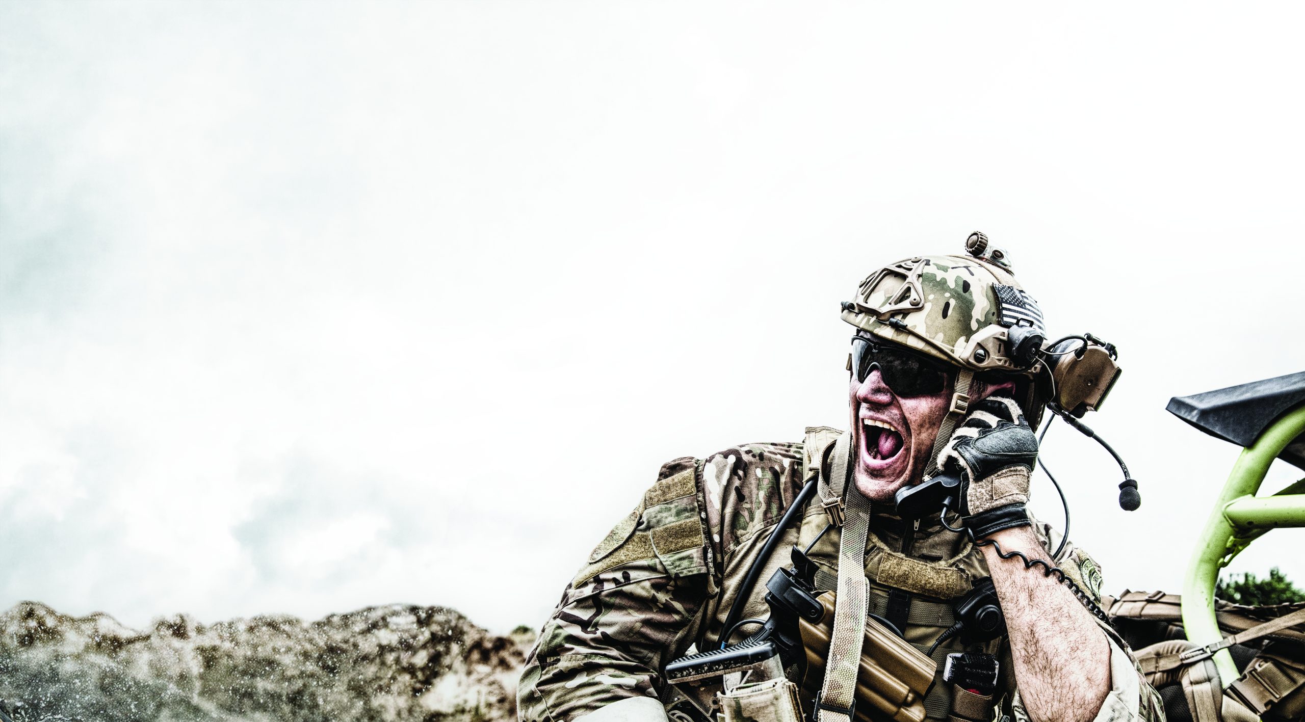 Special forces soldier, military communications operator or maintainer in helmet and glasses, screaming in radio during battle in desert. Calling up reinforcements, reporting situation on battlefield