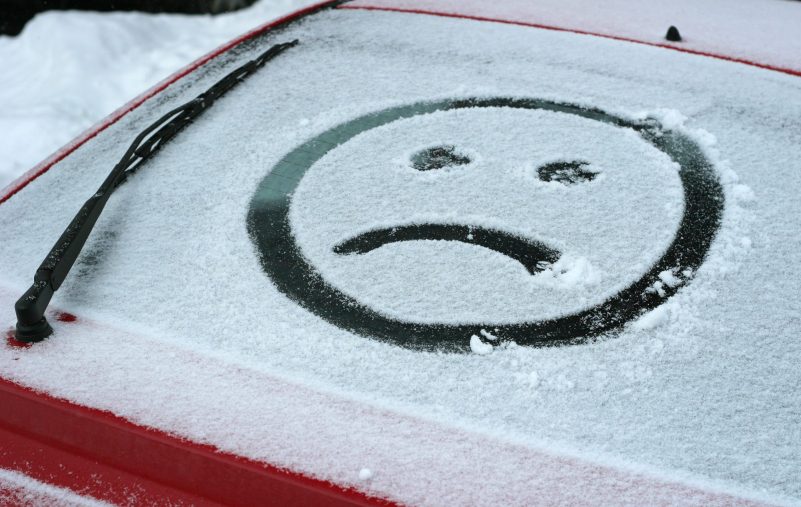 Sad face in snow on car.